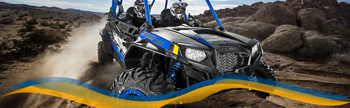 Two people riding a blue Polaris® ATV on a dirt trail while kicking up dust behind them.